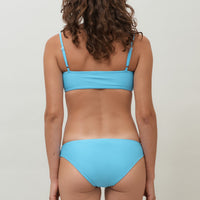 A woman wearing a lake blue sustainable swimwear classic brief style bikini bottom with matching minimalist bikini top.
