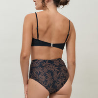 A woman wearing a high-waist sustainable swimwear bottom in a black and brown leaf print.
