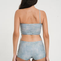 woman wearing minimalist blue green tankini top with rouched side seams and matching low rise swim shorts, sustainable swimwear to swim and surf in.