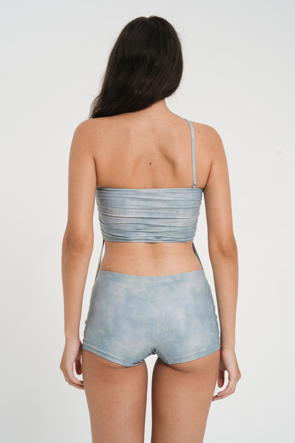 woman wearing a matching set of sea glass blue sustainable swimwear, consisting of a strapless top and low rise mini boy leg swim shorts.
