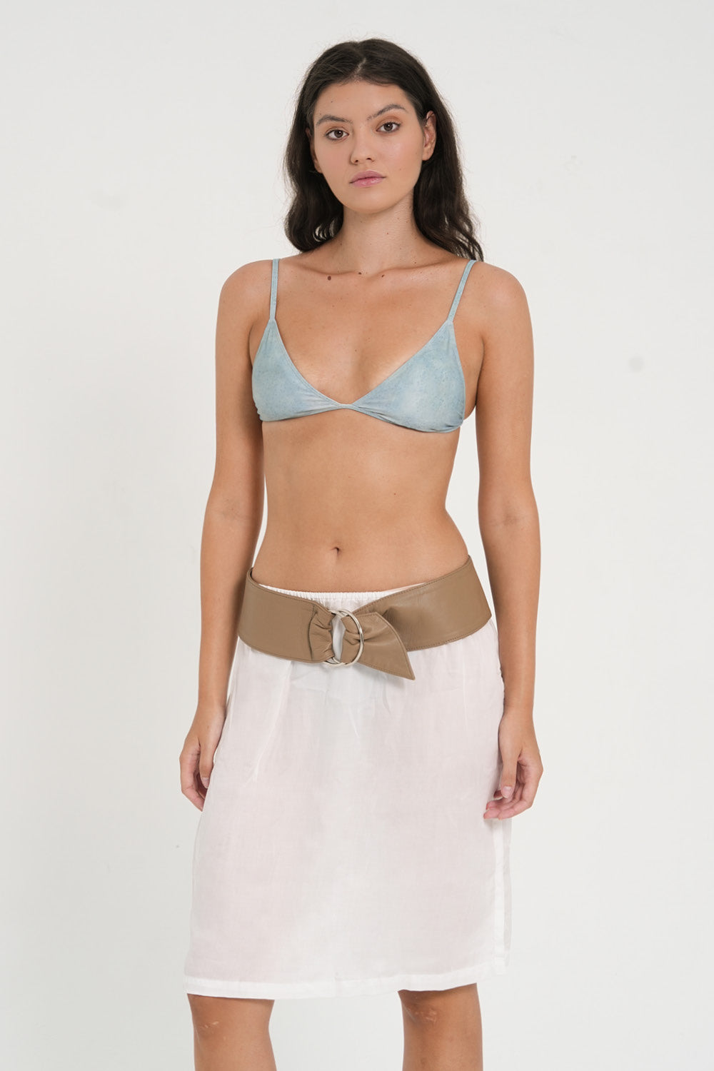 woman wearing fixed triangle bikini top in sea glass print, with minimalist leather belt and white skirt.