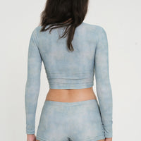 woman wearing blue green long sleeve cropped rashguard and matching low rise swim short, sustainable swimwear for surf and sun protection.