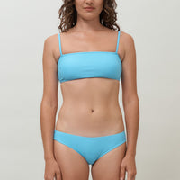 A woman wearing a lake blue sustainable swimwear classic brief style bikini bottom with matching minimalist bikini top.