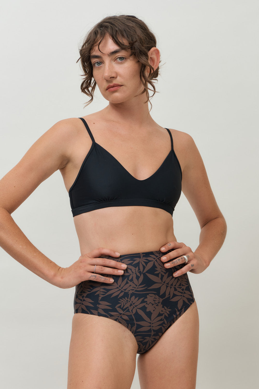A woman wearing a high-waist sustainable swimwear bottom in a black and brown leaf print.