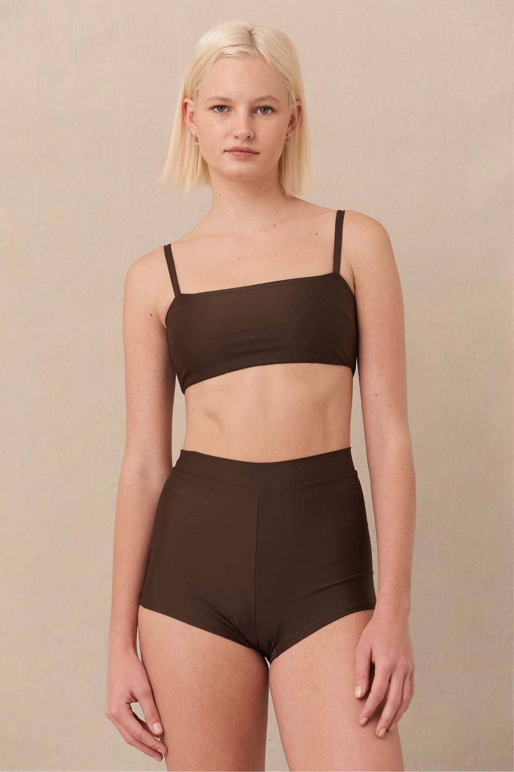 Woman wearing brown high waist surf shorts, sustainable swimwear designed to stay on in the surf, offering supportive coverage and a flattering fit for active beach days.
