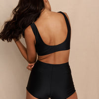 Woman wearing black high waist surf shorts, sustainable swimwear designed to stay on in the surf, offering supportive coverage and a flattering fit for active beach days.