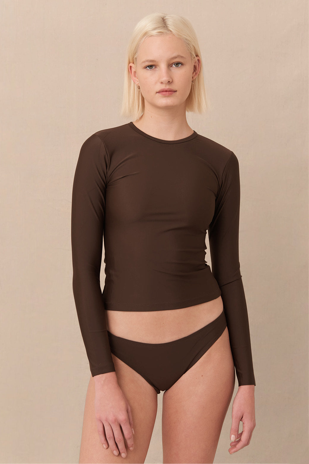 A woman wearing a brown sustainable swimwear classic brief style bikini bottom with a long sleeve rashguard.