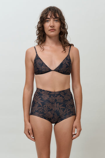 Woman wearing black and brown leaf print high waist surf shorts, sustainable swimwear designed to stay on in the surf, offering supportive coverage and a flattering fit for active beach days.