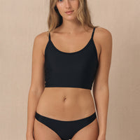 A woman wearing a black sustainable swimwear bikini top and bottom. The bottom is a classic brief style with medium coverage.