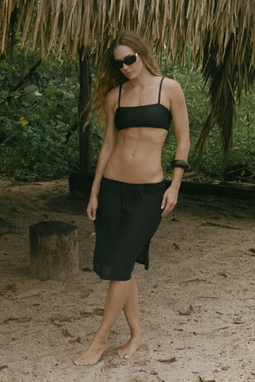 Woman in black bikini top and sheer black skirt standing on the beach