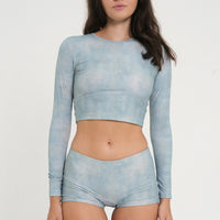 woman wearing a matching set of sea glass blue sustainable swimwear, consisting of cropped rashguard and low rise mini boy leg swim shorts.
