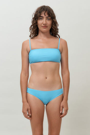A woman wearing a lake blue sustainable swimwear classic brief style bikini bottom with matching minimalist bikini top. 
