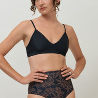 A woman wearing a high-waist sustainable swimwear bottom in a black and brown leaf print.