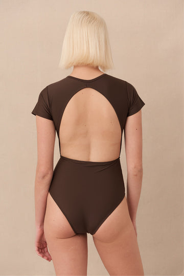 Woman wearing brown Chacahua Surf Suit — a sustainable one piece swimsuit with a flattering cut-out back, cap sleeves for sun protection and designed to stay put in the surf. Minimalist swimwear meets high-performance 