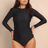 woman wearing sustainable black long sleeve minimalist rashguard for sun protection and surfing.